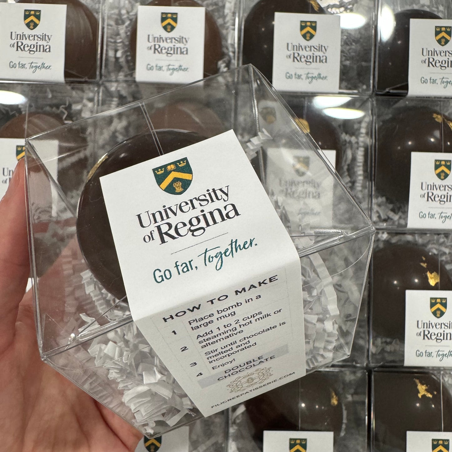 A Hot Chocolate Bomb with a sticker featuring the University of Regina logo.
